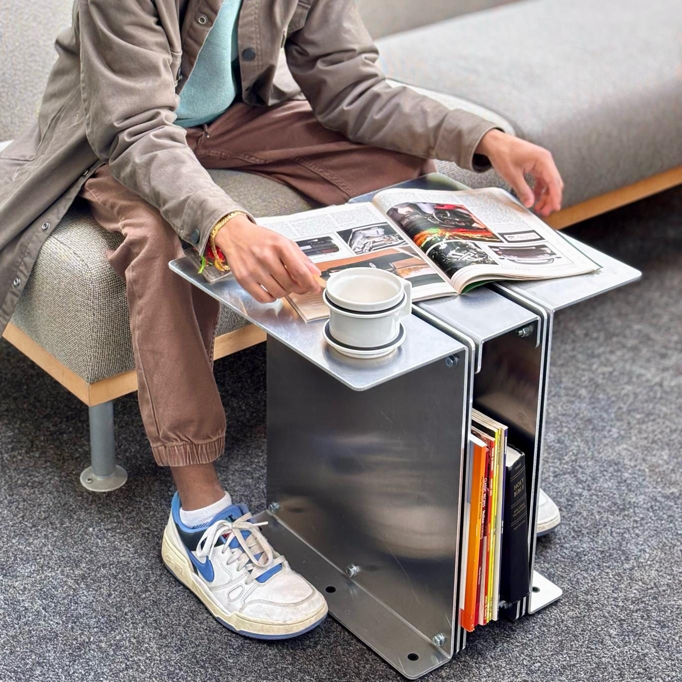 3082 beside a sofa, holding a magazine and mug
